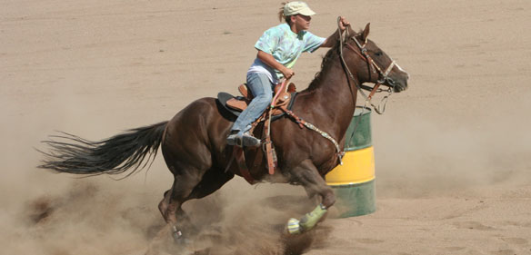 Cowboy riding horse around a green and yellow barrel