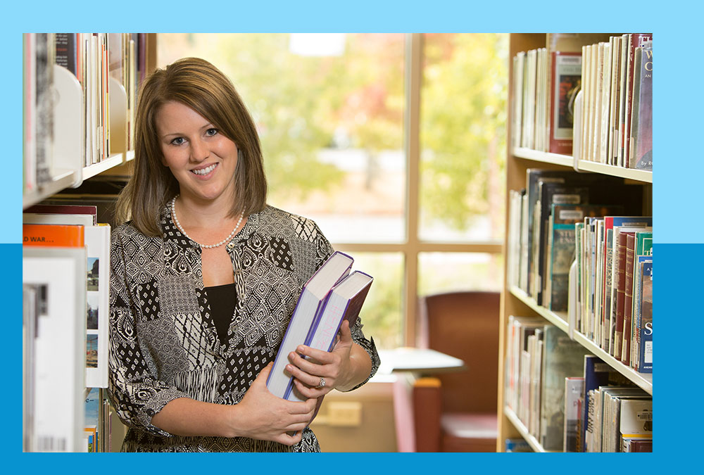 Female student holding a couple of books while standing in the library.